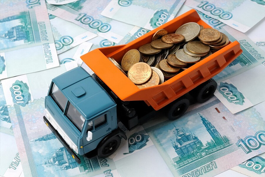 Игрушечный КАМАЗ с монетами в кузове стоит на денежных купюрах